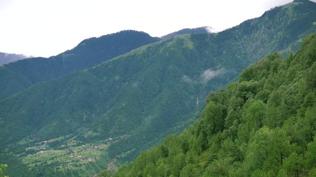 panning shot of plant and tree covered mountains with clouds rolling over them shot at McLeodganj