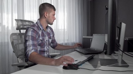 Handsome IT office worker using two computers working on a project. Young computer programmer working online. Attractive man studying online. Internet concept