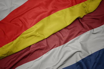 waving colorful flag of netherlands and national flag of south ossetia.