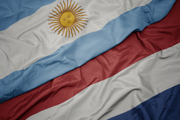 waving colorful flag of netherlands and national flag of argentina.