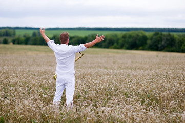 saxophonist in a white suit stands in the field. Flight of the soul, philosophy of freedom