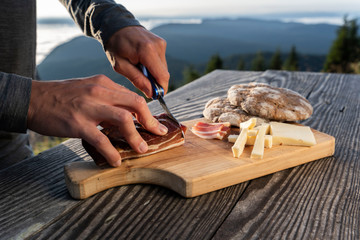 Man slice up delicious South Tyrolean smoked bacon and cheese with flat bread lying on a rustic...