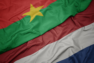 waving colorful flag of netherlands and national flag of burkina faso.