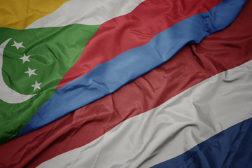 waving colorful flag of netherlands and national flag of comoros.