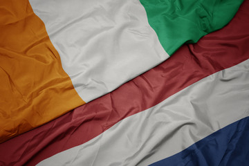 waving colorful flag of netherlands and national flag of cote divoire.