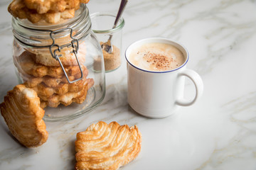 Italienische Blätterteig Fächer Kekse mit Einmachglas und Becher Kaffee auf Marmor Hintergrund
