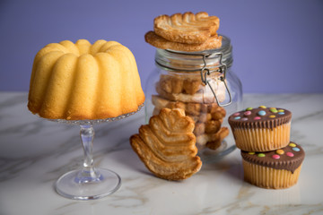 Gugelhupf Kuchen, Muffins und Italienische Blätterteig Fächer Kekse als Gebäck Auswahl Büffet auf Marmor Tisch und Lila Hintergrund