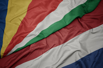 waving colorful flag of netherlands and national flag of seychelles.