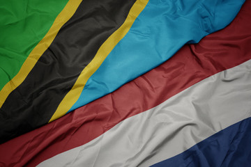 waving colorful flag of netherlands and national flag of tanzania.