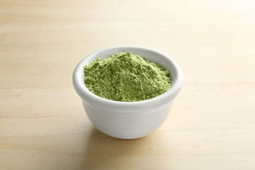 Bowl of wheat grass powder on wooden table