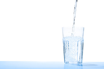 Pouring water into glass against blue background, space for text. Refreshing drink