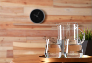 Tray with jug and glasses of water on wooden table in room, space for text. Refreshing drink