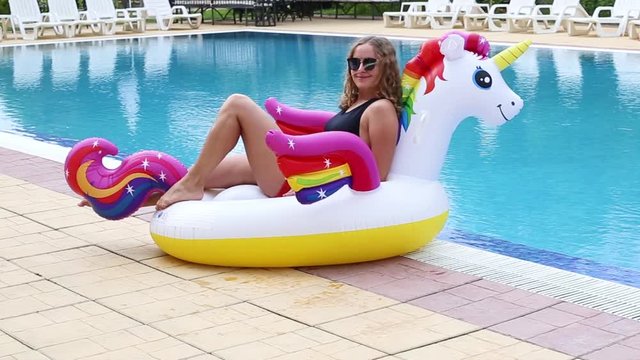 Woman relaxing on inflatable unicorn near swimming pool