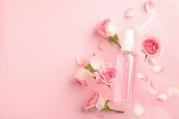 Flat lay composition with rose essential oil and flowers on pink background, space for text