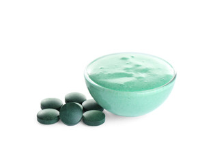 Freshly made spirulina facial mask in bowl and pills on white background