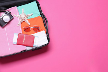 Open suitcase with beach objects on pink background, top view. Space for text