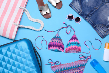 Suitcase and beach objects on blue background, flat lay