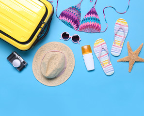 Yellow suitcase and beach objects on blue background, flat lay