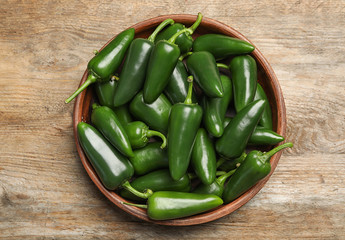 Bowl with green hot chili peppers on wooden table, top view