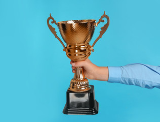 Boy holding golden winning cup on blue background, closeup