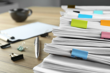 Stack of documents with binder clips and pen on wooden table, closeup view