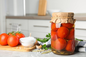 Jar with pickled tomatoes and vegetables on grey table in kitchen. Space for text