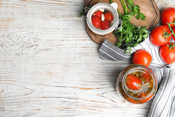 Flat lay composition with pickled tomatoes in glass jars on white wooden table, space for text