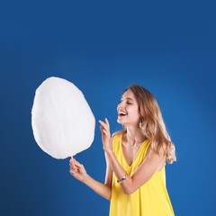 Happy young woman with cotton candy on blue background