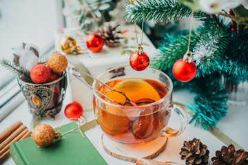 mug of hot black tea near the window, spruce branch with a red ball, cones, Christmas decor,