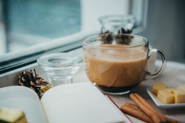 1 Cup of coffee with milk near the window, book, cinnamon, cheese, cone, candle,