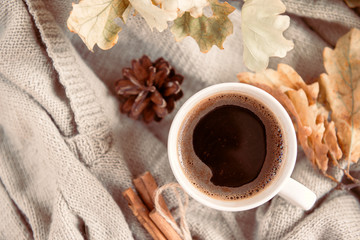 1 mug of hot black coffee on the background of a gray sweater, yellow dry fallen autumn leaves, top view