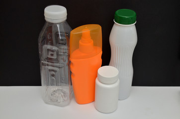 Four plastic bottles, white and orange, on a black and white background. Concept of reducing amount of a plastic used