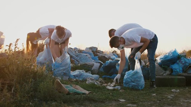 Group of eco volunteers cleaning up area of dump near the field during sunset