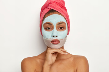 Calm young female model enjoys daily skincare regime, applies soothing mask on face, reduces...