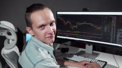 Male computer programmer smiling to the camera while working late at the office. Young cheerful IT office employee working on a project late at night. Freelance, business concept