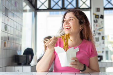 Close-up portrait of young pretty girl eating chinese noodles with wooden chopsticks sitting in a cafe. Concept of hunger and satiety.