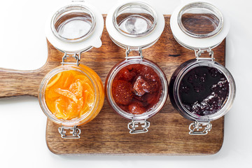 open jars with different jam on a wooden board