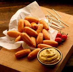 Pile of Cocktails sausages on wooden board with mustard
