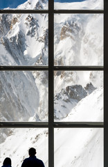 Silhouette of two people looking at majestic mountain landscape through a huge window high in the Alps