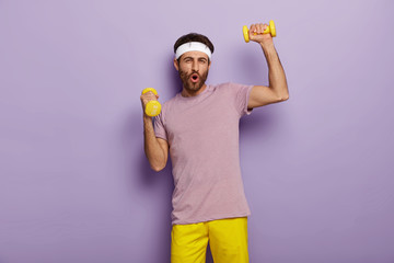 Funny man has fun, exercises with dumbbells, dressed in active wear, motivated for healthy...