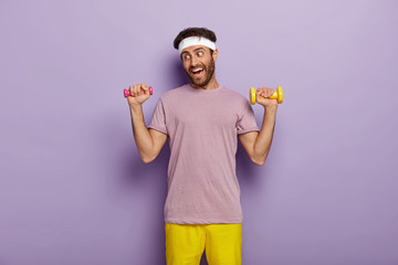 Sport and recreation concept. Funny sportsman exercises with dumbbells, wants to have strong...