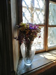 Kermek dried flowers autumn flowers in a glass vase against the background of an old tattered window