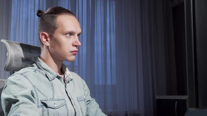 Sliding shot of a male freelancer working late in the evening using two computers. Young programmer working on a project in a dark room. Intelligence, computers concept