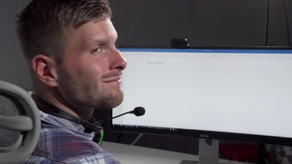 Handsome call center operator smiling to the camera after typing on his computer. Cropped rear view shot of a male customer support manager wearing headset with microphone