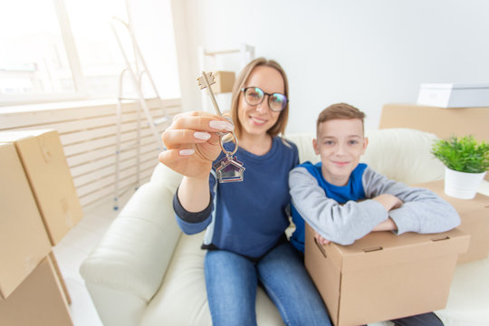 Blurred positive mom and son are sitting on the couch and showing the keys to the new apartment. The concept of home buying on credit and housewarming. Single parent