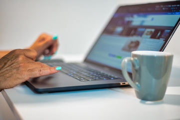 Woman hands using laptop with cup of coffee on the side, lateral view