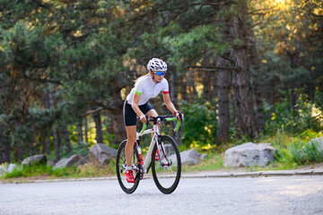 Naklejka premium Young Woman Cyclist Riding Road Bicycle on the Free Road in the Forest at Hot Summer Day. Healthy Lifestyle Concept.