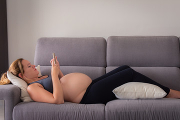 Full length of a pregnant woman lying on the sofa using her smartphone