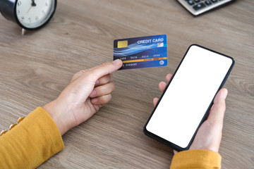 Women hands holding Mobile Phone with blank screen and Credit Card on office desk and using mobile phone for Online Shopping, Internet Banking, Online Trading, E Commerce Concept. with clipping path