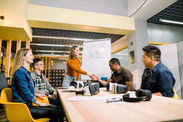Business team in casual wear having meeting about new project of virtual reality simulator. Young woman in casual wear shaking hands with colleagues in the modern loft office